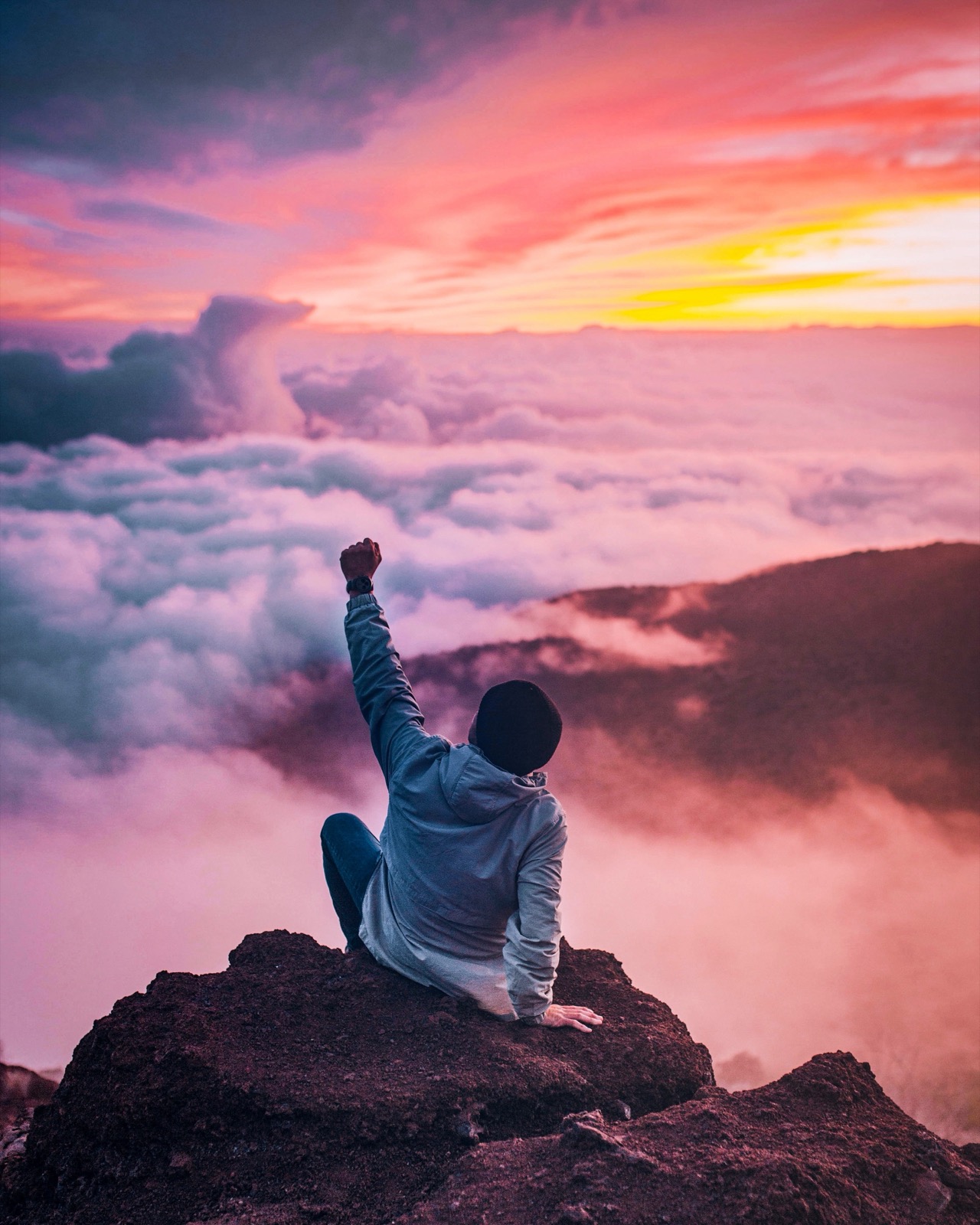 Person auf einem Gipfel über dem Wolkenmeer im Abendrot